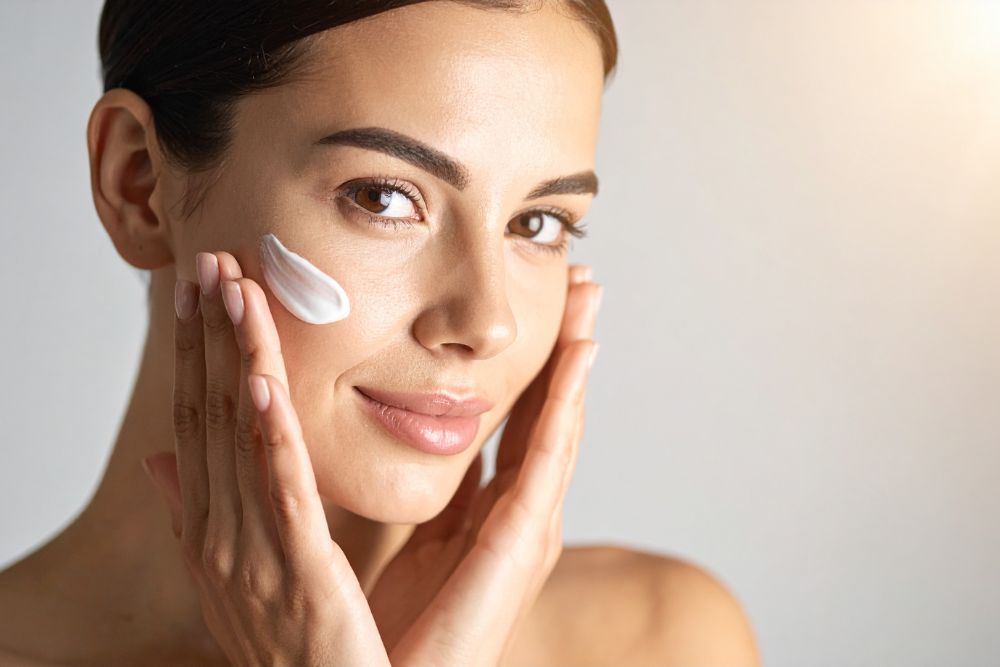 Mujer aplicando crema hidratante reparadora en la mejilla durante la noche de descanso de skin cycling
