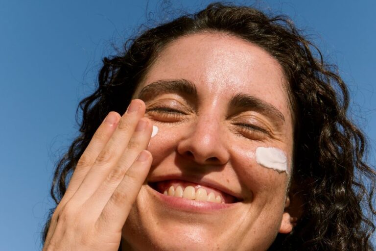 ujer sonriendo al extender crema fotoprotectora en las mejillas