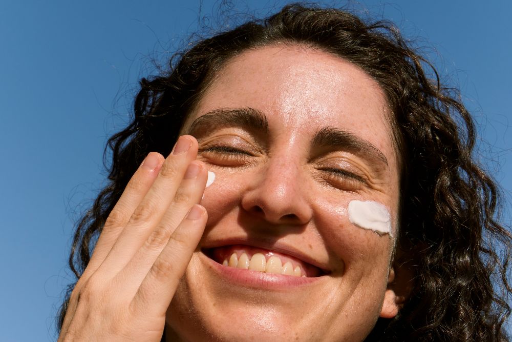 ujer sonriendo al extender crema fotoprotectora en las mejillas