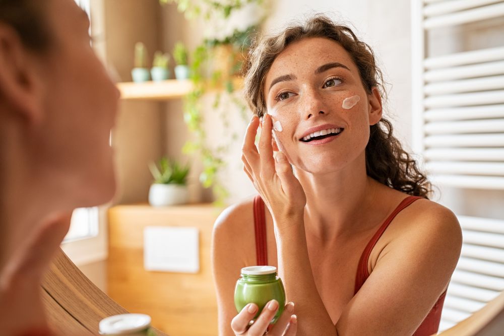 Mujer aplicando tratamiento facial frente al espejo del baño.