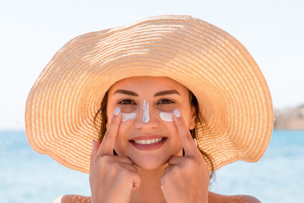 Mujer con sombrero de paja aplicando protector solar en mejillas y nariz