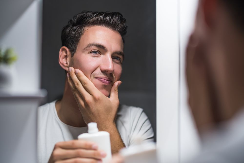 Hombre sonriendo frente al espejo tras su rutina de cuidado facial